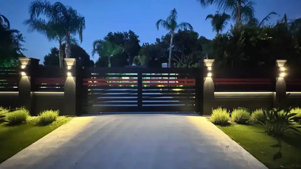 Black aluminum sliding driveway gate between lit columns at dusk, San Fernando Valley project