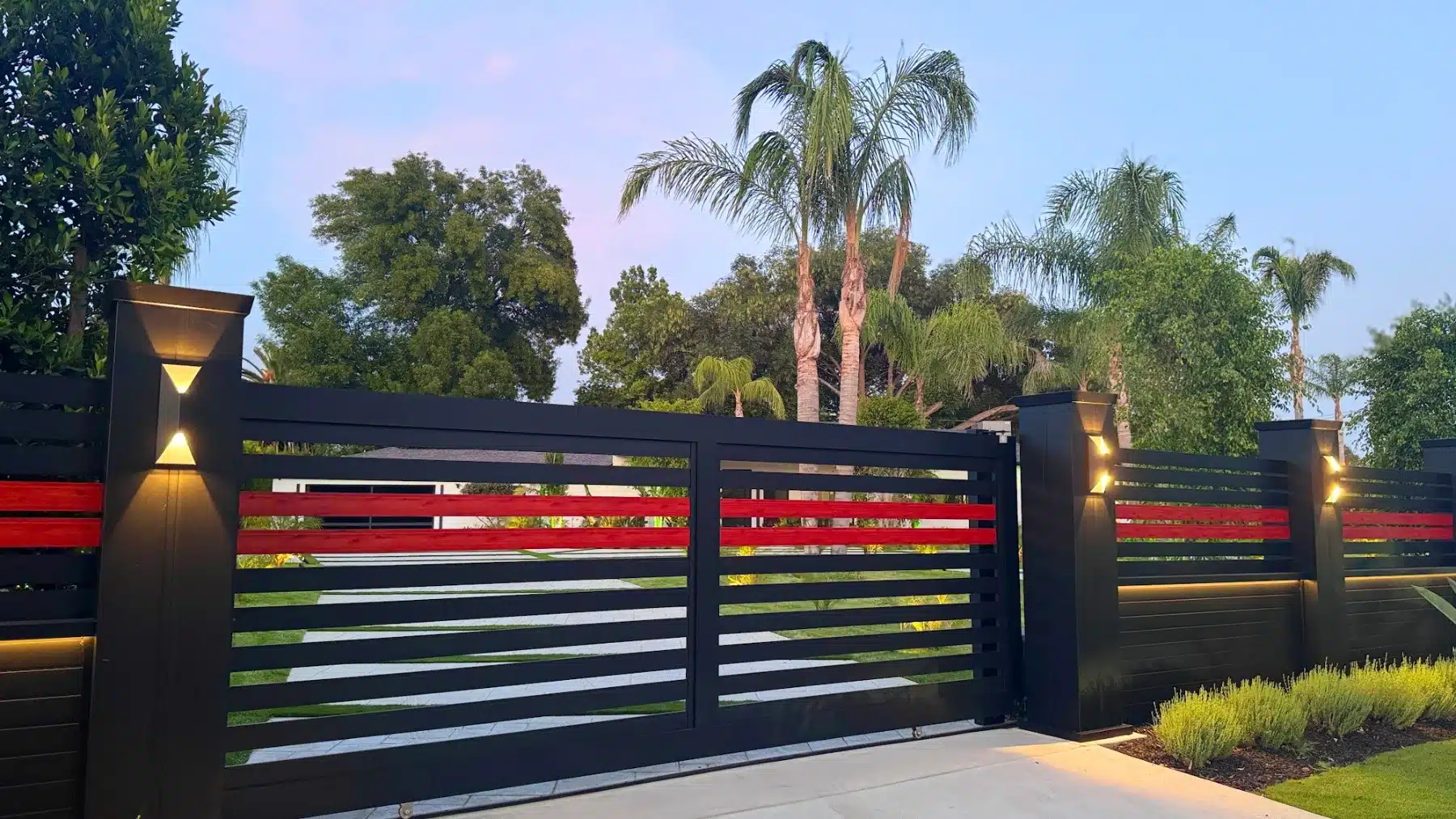 Horizontal-slat aluminum driveway gate with wood-look accent rails and lit columns