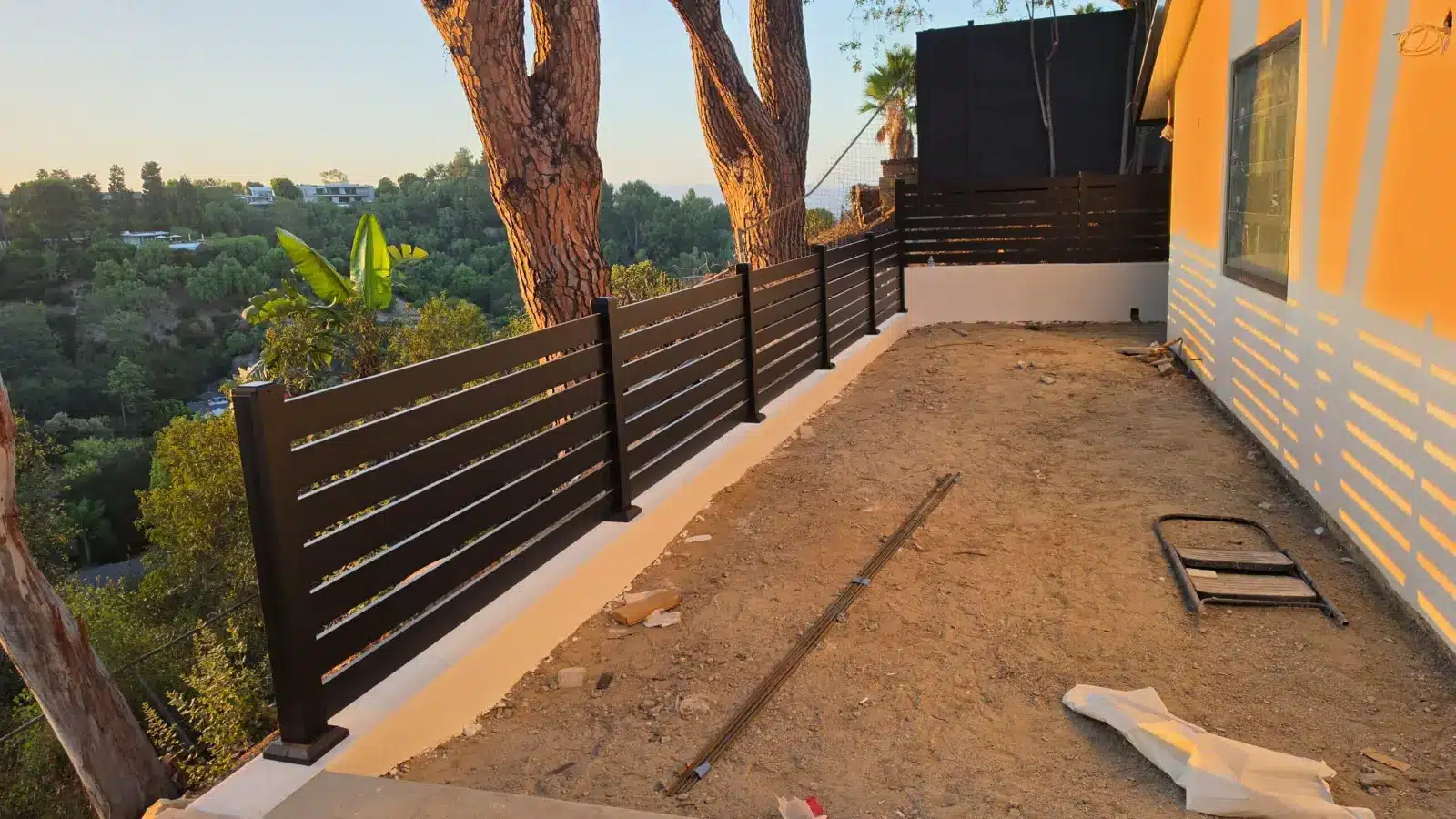 Black horizontal aluminum fence running along the edge of a hillside yard